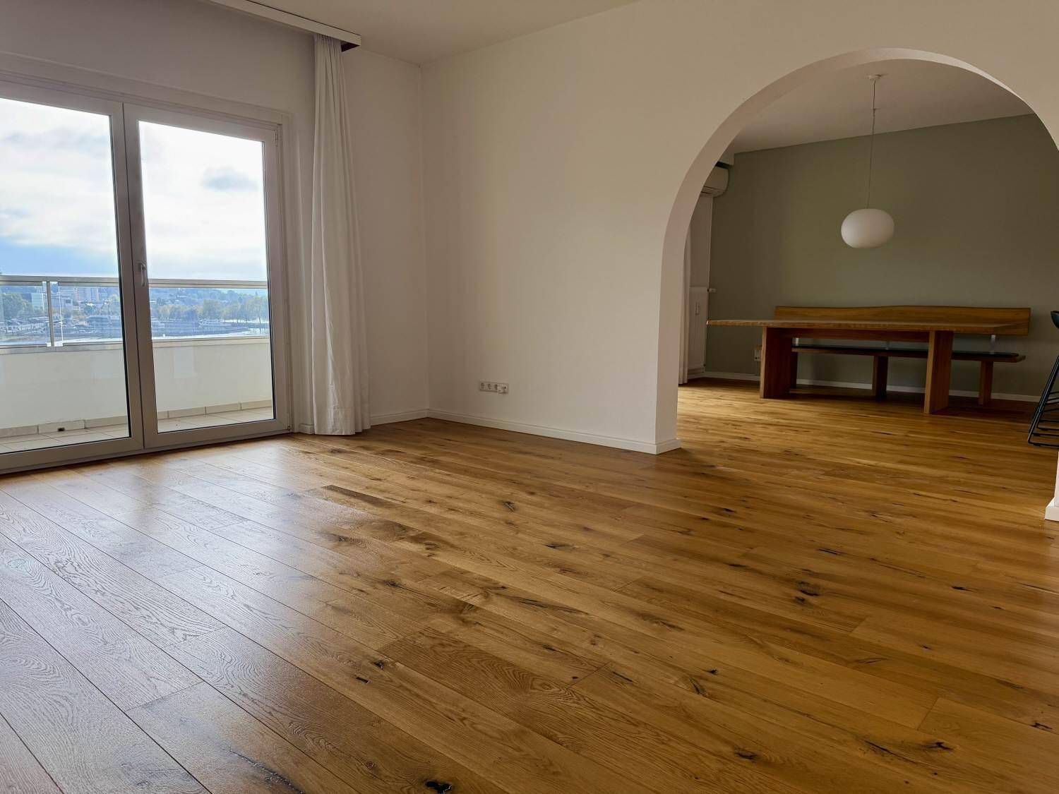 Geräumiges Wohnzimmer mit Holzboden, einem eleganten Bogen und Balkonzugang.