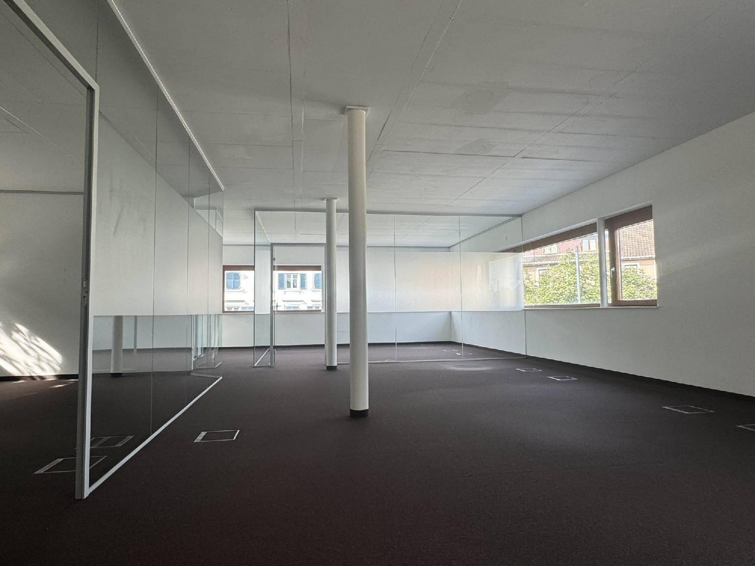 Großes, offenes Büro mit Teppichboden, Säulen und modernen Glaswänden, die den Raum strukturieren.