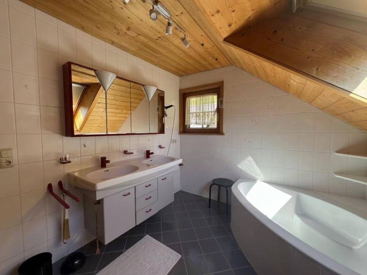 Badezimmer mit Doppelwaschbecken, Spiegelschrank und Eckbadewanne unter Dachschräge.