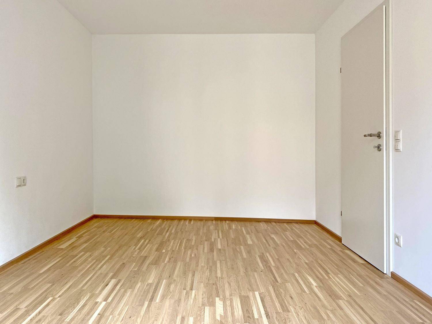 Leeres Zimmer mit Parkettboden und weiß gestrichenen Wänden, bereit zum Einzug.