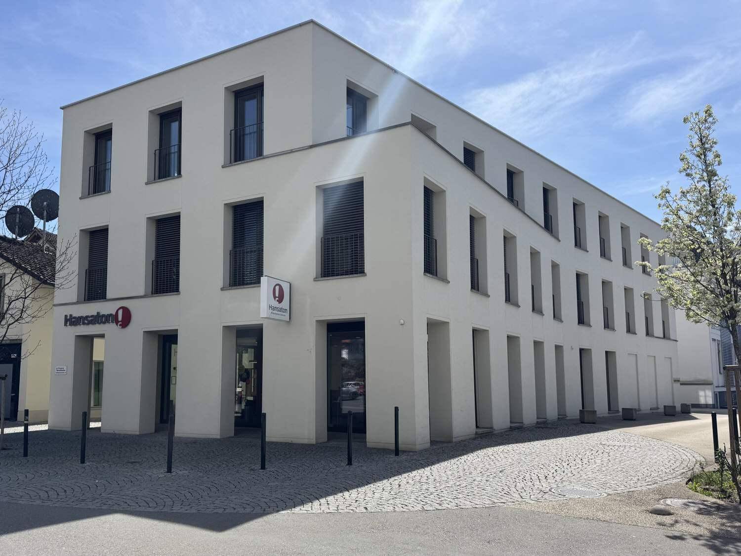 Ansicht des modernen Gebäudes mit mehreren Etagen, großen Fenstern und Rollläden in einer städtischen Umgebung.