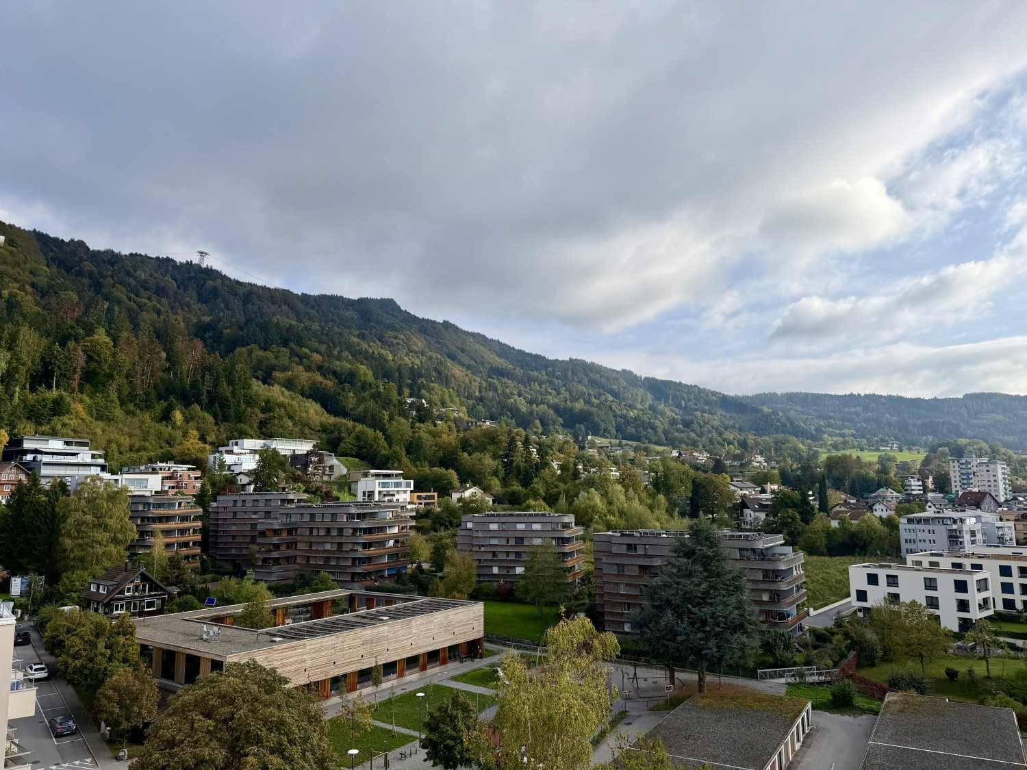 Panoramablick auf eine moderne Wohnsiedlung mit viel Grün und bewaldeten Hügeln.