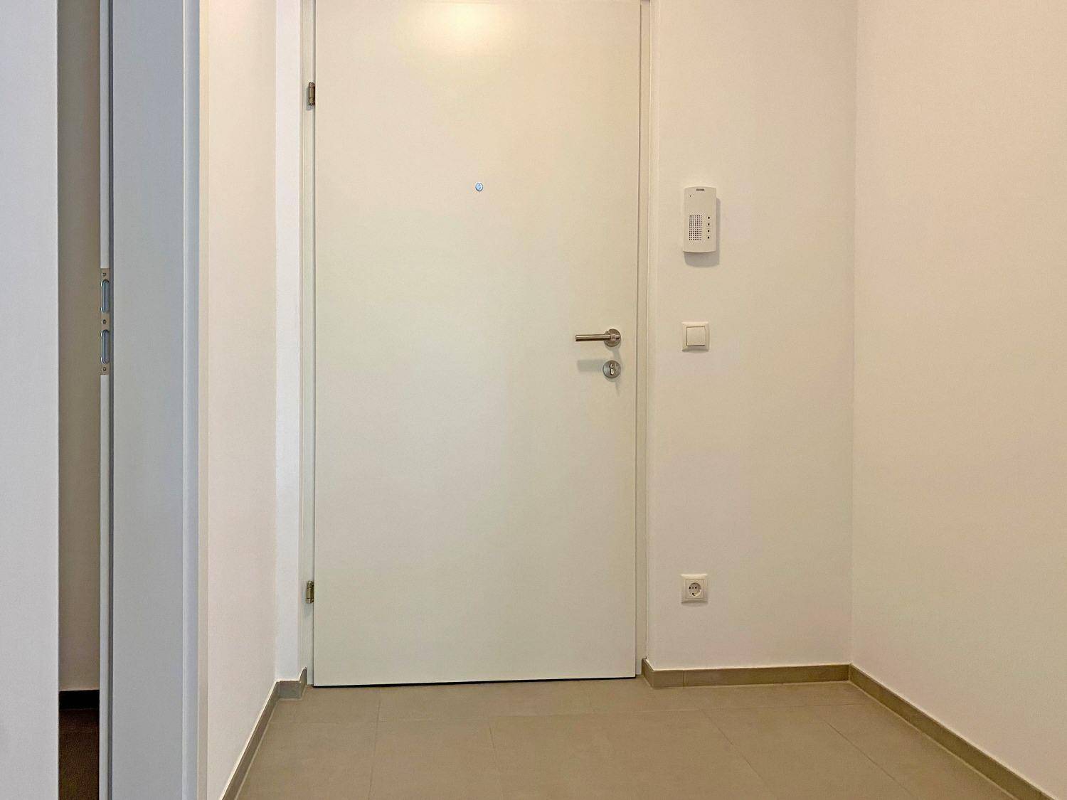 Eingangsbereich mit Fliesenboden, weißer Tür und Gegensprechanlage.