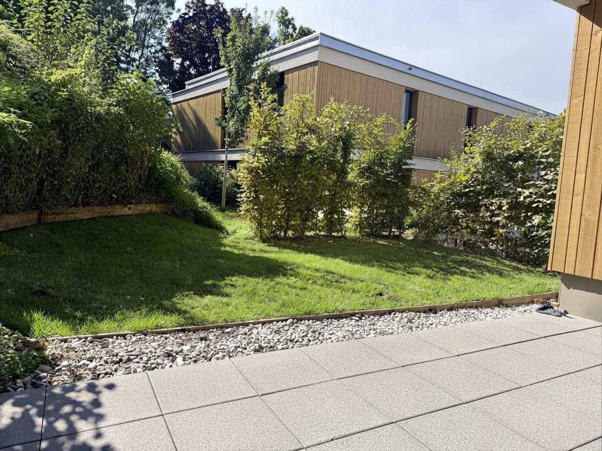 Gepflegter Gartenbereich mit Rasenfläche und gepflasterter Terrasse vor dem Gebäude.