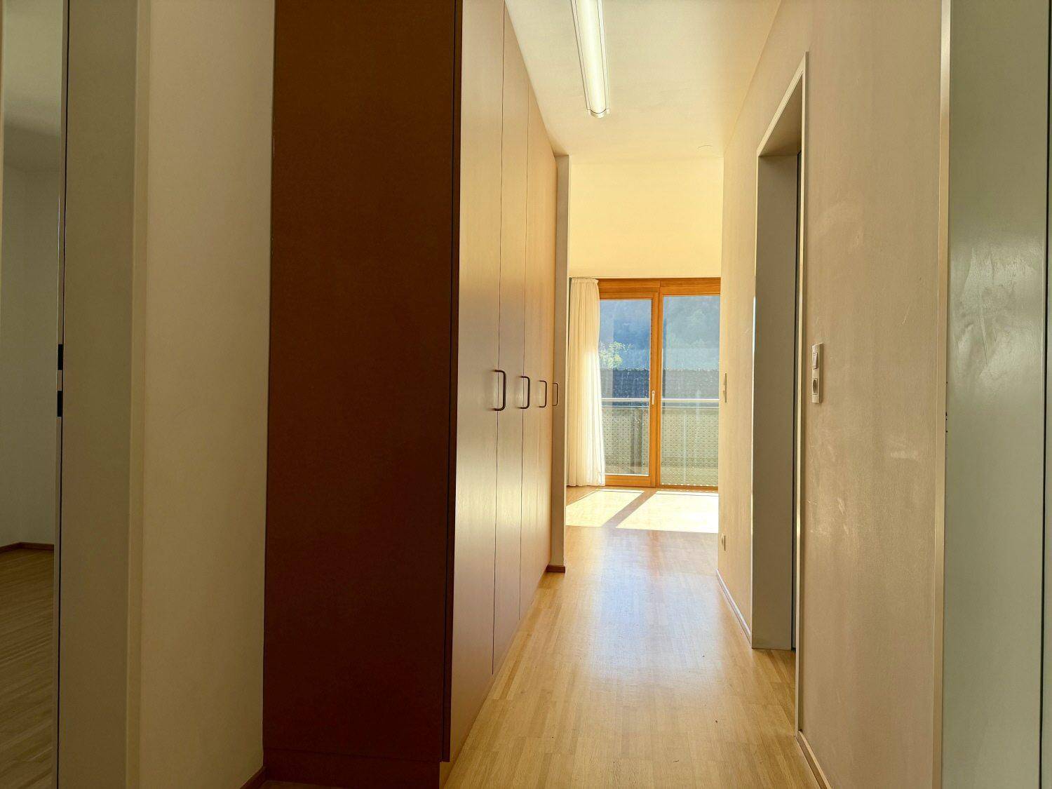 Heller Flur mit Einbauschränken und Holzboden, der zum lichtdurchfluteten Wohnbereich führt.