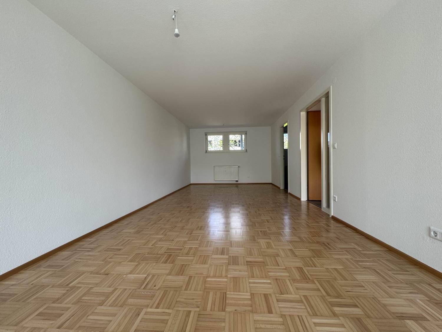 Heller Raum mit Parkettboden, weißen Wänden und einem Fenster, ideal als Wohnbereich.