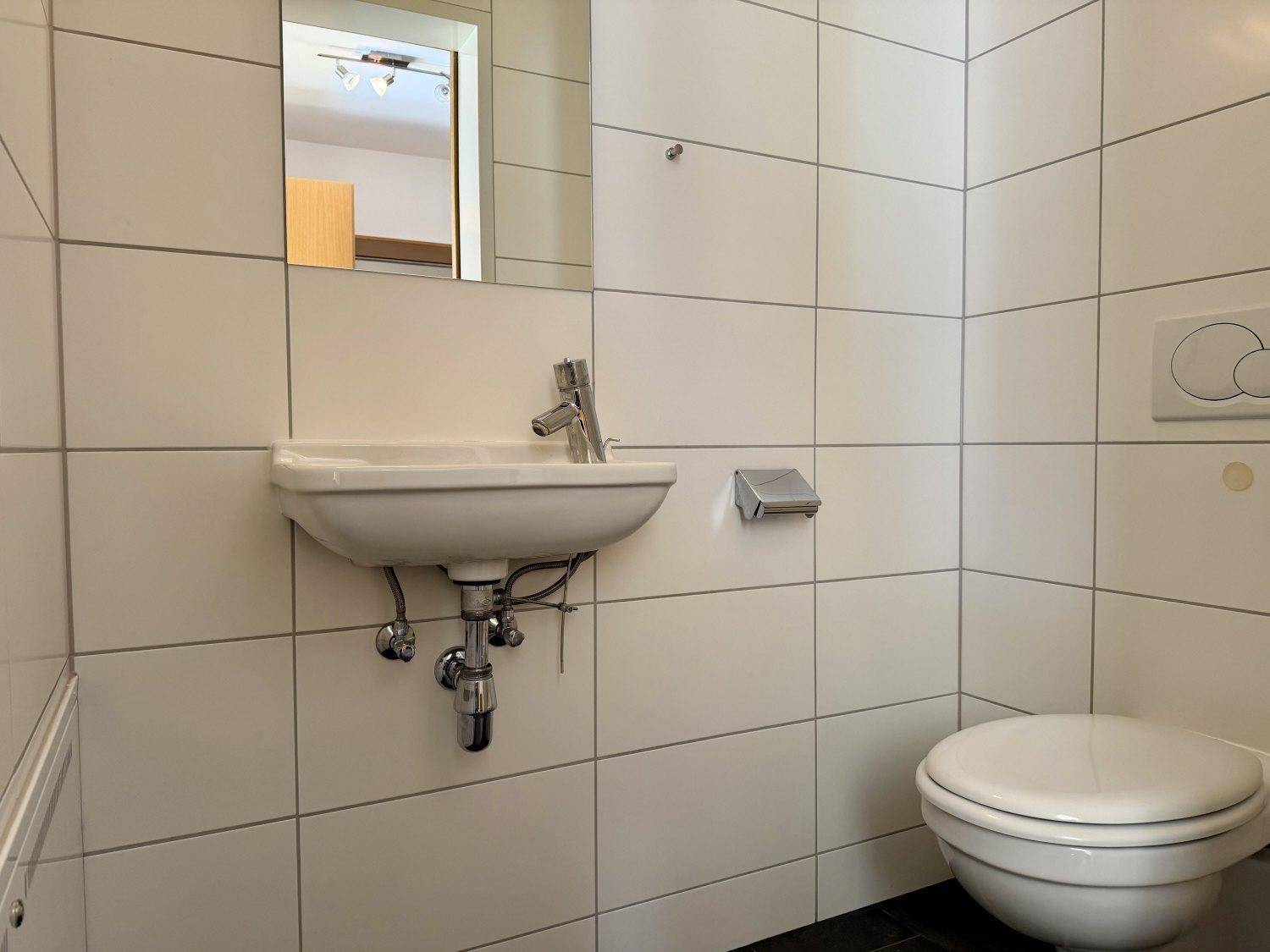 Kleines Gäste-WC mit weißen Fliesen, wandhängender Toilette und einem Waschbecken.