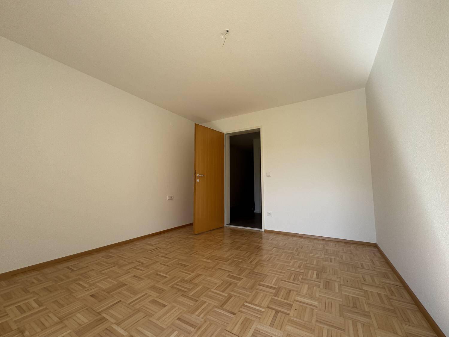 Leeres Schlafzimmer mit Parkettboden und weißen Wänden, bereit zur individuellen Gestaltung.