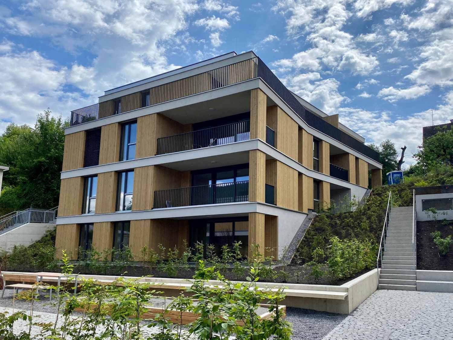 Modernes Wohngebäude mit Holzfassade, Balkonen und gepflegter Außenanlage.