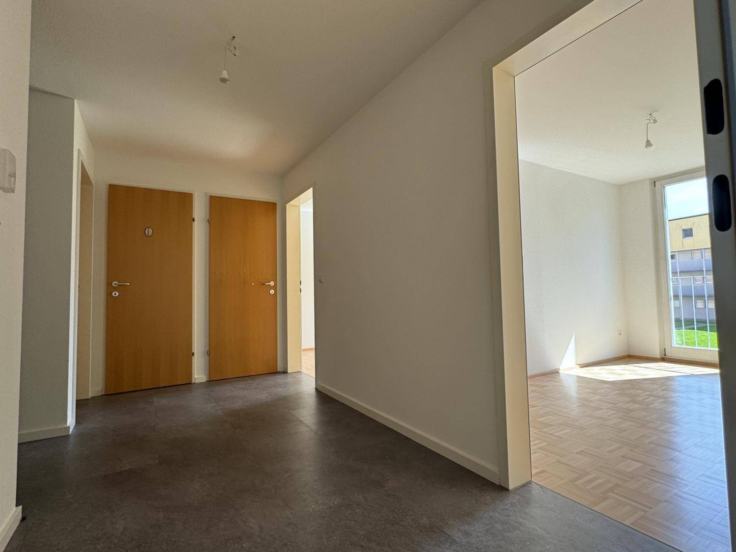 Heller Flur mit Fliesenboden, weißen Wänden und Holztüren, der zu weiteren Räumen führt.