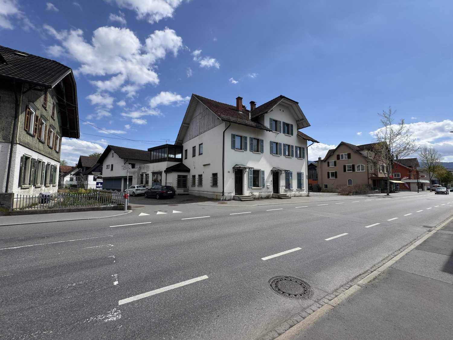 Ansicht des Wohnhauses von der Straße mit umliegenden Gebäuden und einem Parkplatz.