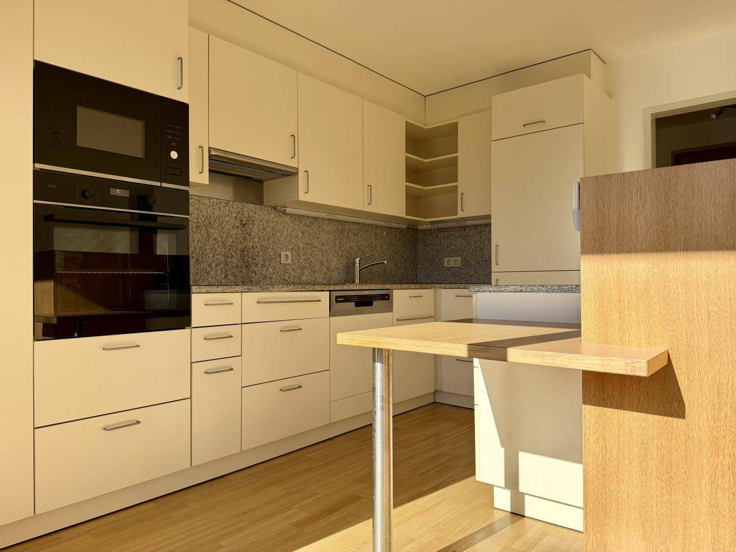 Moderne Einbauküche mit hellen Schränken, Granitarbeitsplatte und integrierten Geräten.
