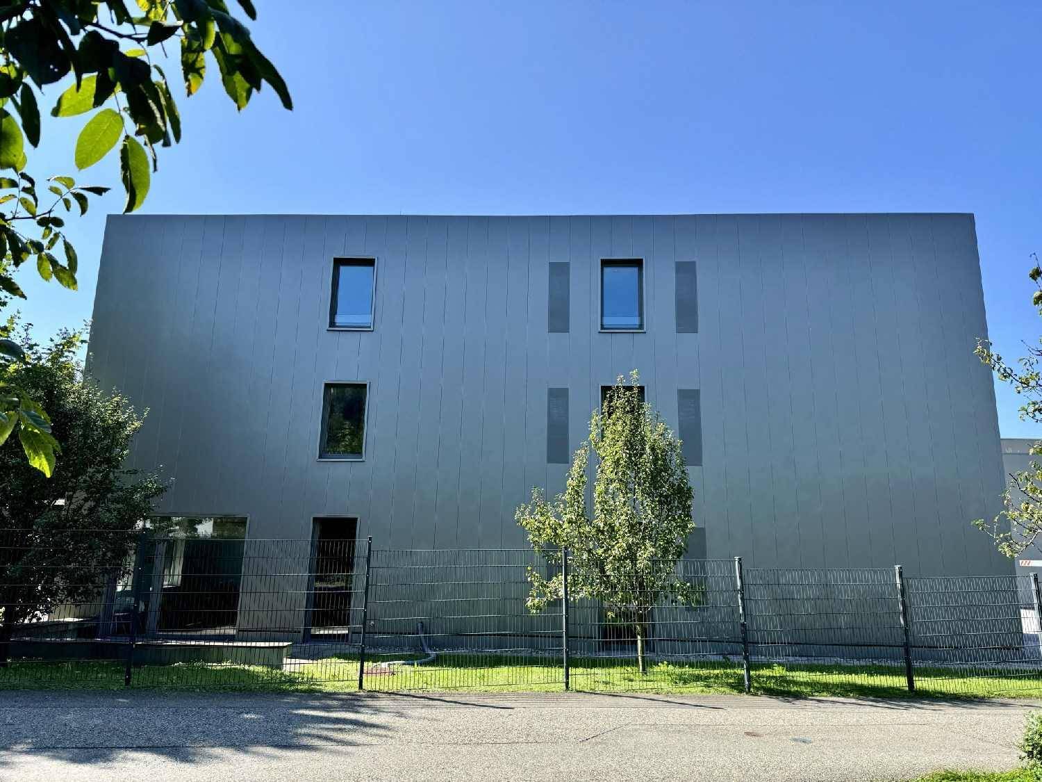 Rückansicht des modernen Bürogebäudes mit grauer Fassade und symmetrisch angeordneten Fenstern.