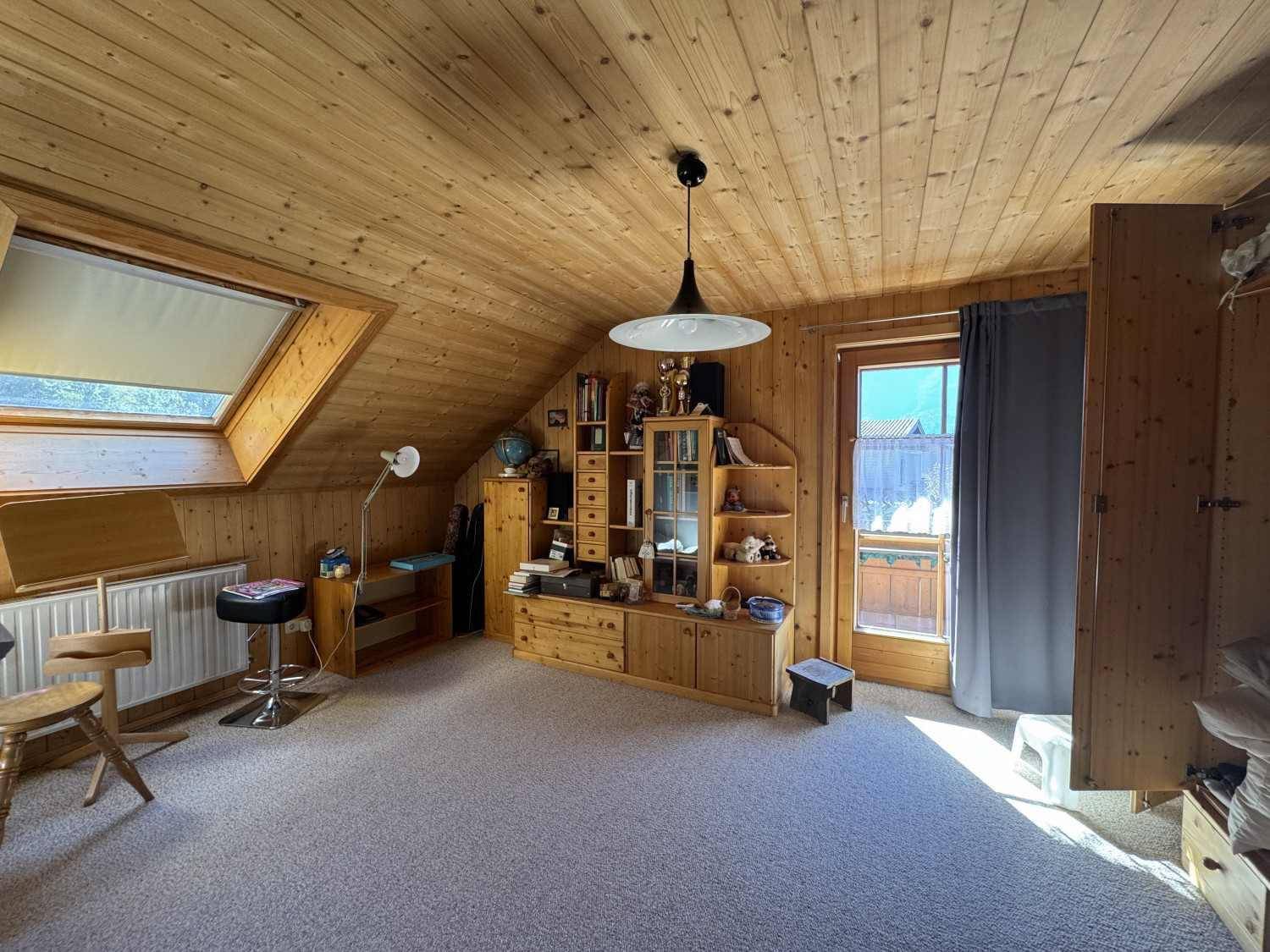 Helles Zimmer im Dachgeschoss mit Teppichboden, Holzdachschrägen und Balkonzugang.
