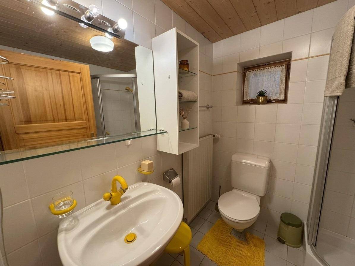 Helles Badezimmer mit weißen Fliesen, gelben Akzenten, Waschbecken, Toilette und Dusche.