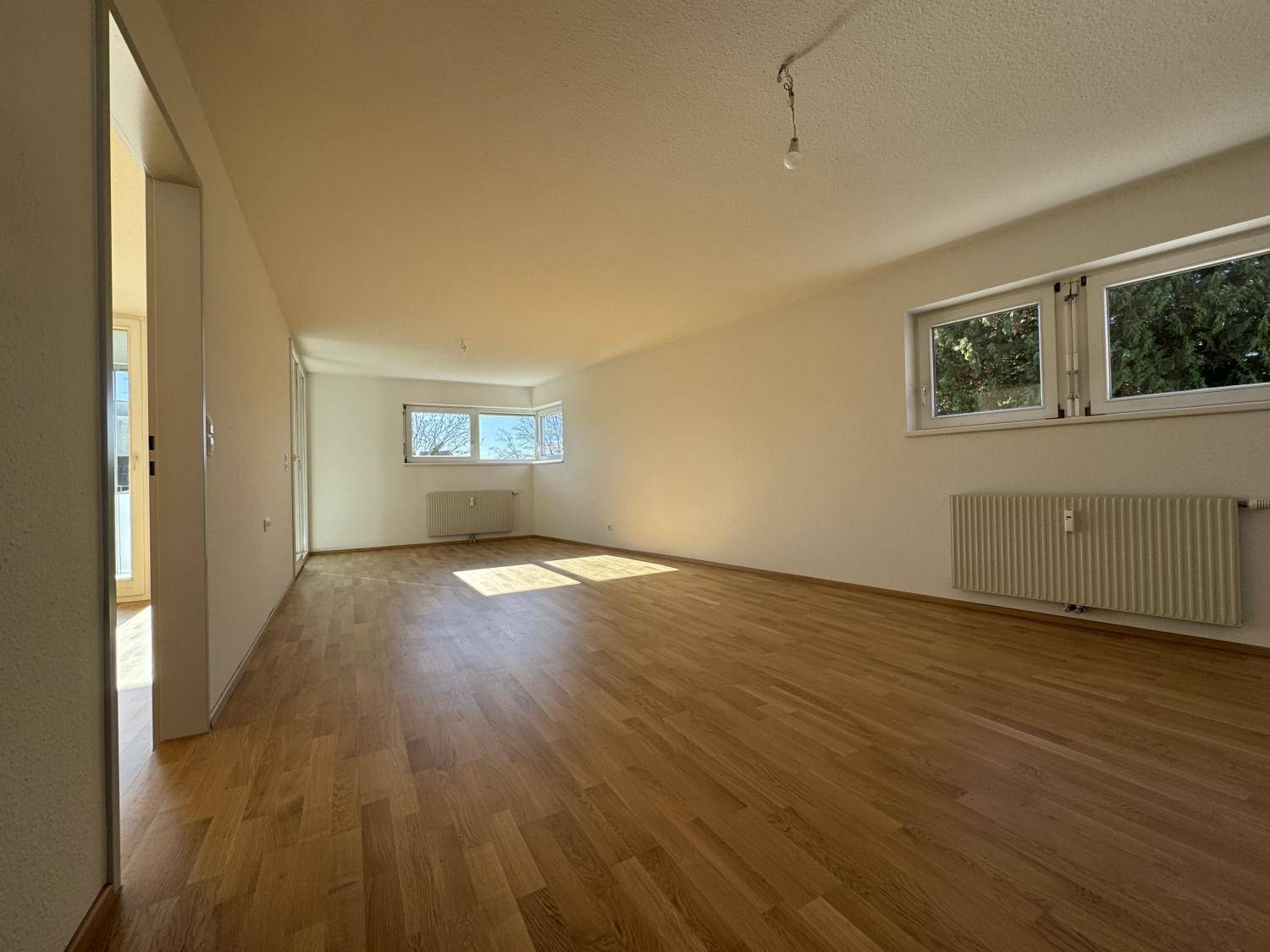 Geräumiges, helles Wohnzimmer mit Parkettboden und mehreren Fenstern für viel Tageslicht.