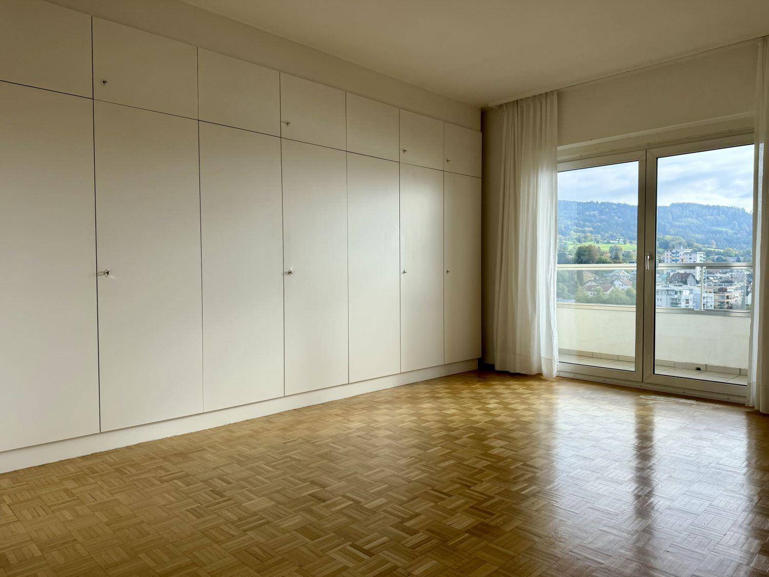 Helles Schlafzimmer mit Parkett, Einbauschränken und schöner Aussicht vom Balkon.
