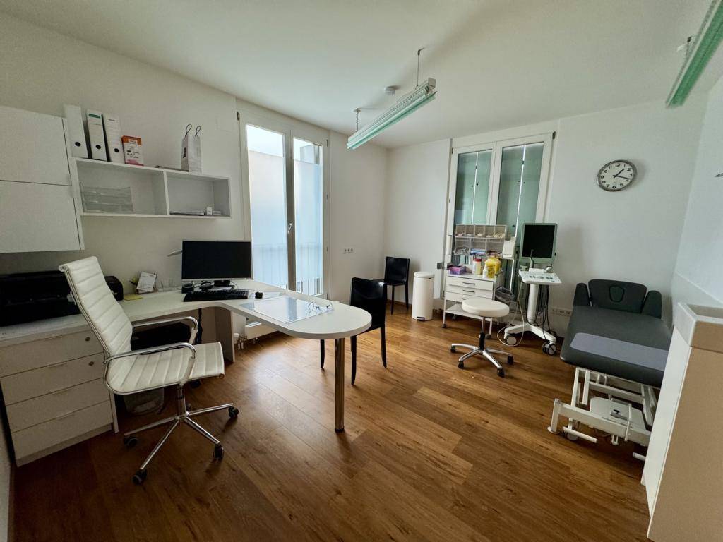 Geräumiges Büro oder Behandlungszimmer mit Holzboden, Schreibtisch und medizinischer Ausstattung, hell und modern.