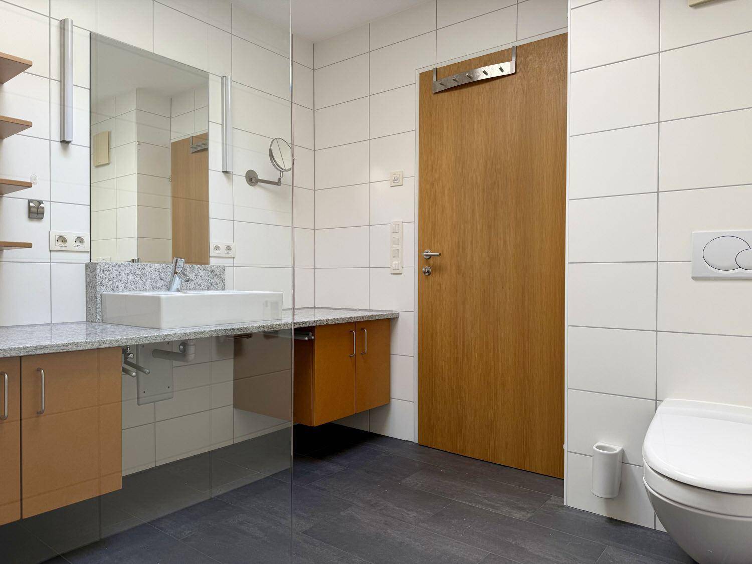 Modernes Badezimmer mit weißen Fliesen, Granitwaschtisch und begehbarer Dusche.