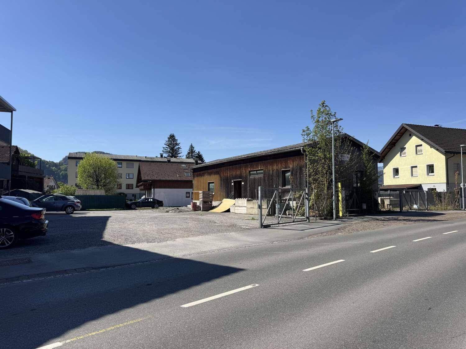 Seitenansicht des Holzgebäudes mit angrenzendem Parkplatz und einer malerischen Berglandschaft im Hintergrund.