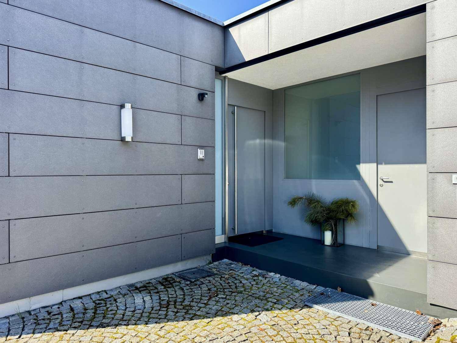 Moderner Eingangsbereich des Hauses mit grauer Fassade und gepflastertem Vorplatz.