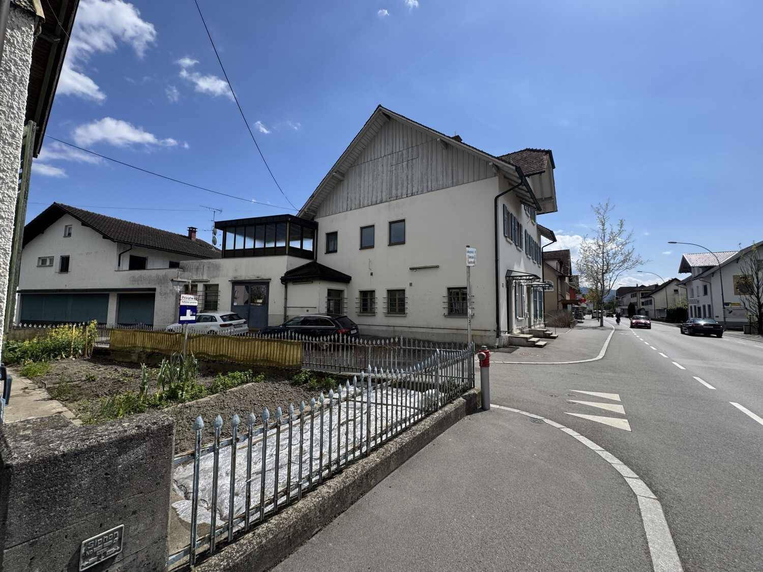 Seitenansicht des Gebäudes mit einem kleinen, eingezäunten Grundstück und angrenzender Straße.