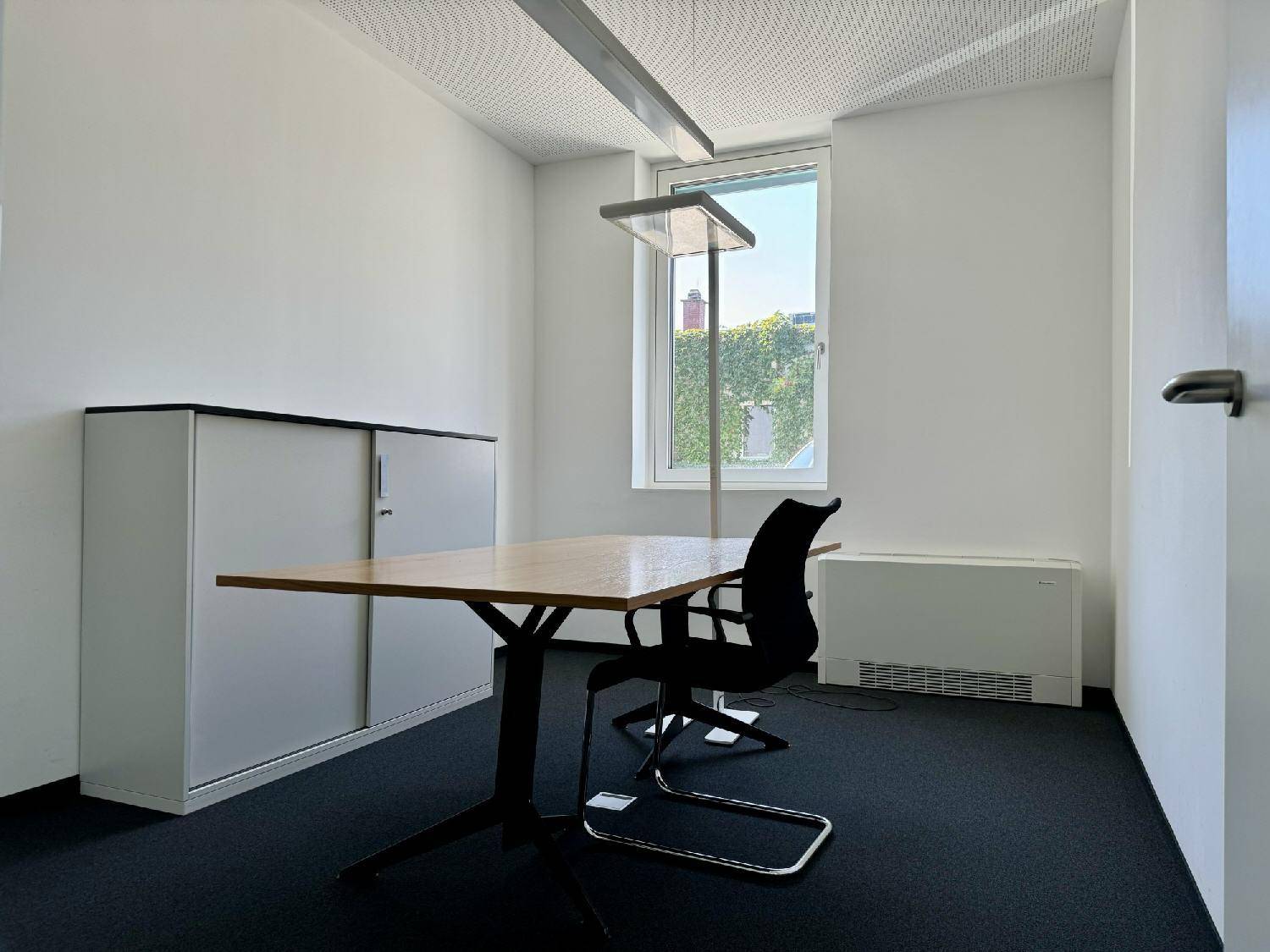 Helles Einzelbüro mit modernem Schreibtisch, Bürostuhl und Schrank, ausgestattet mit Teppichboden.