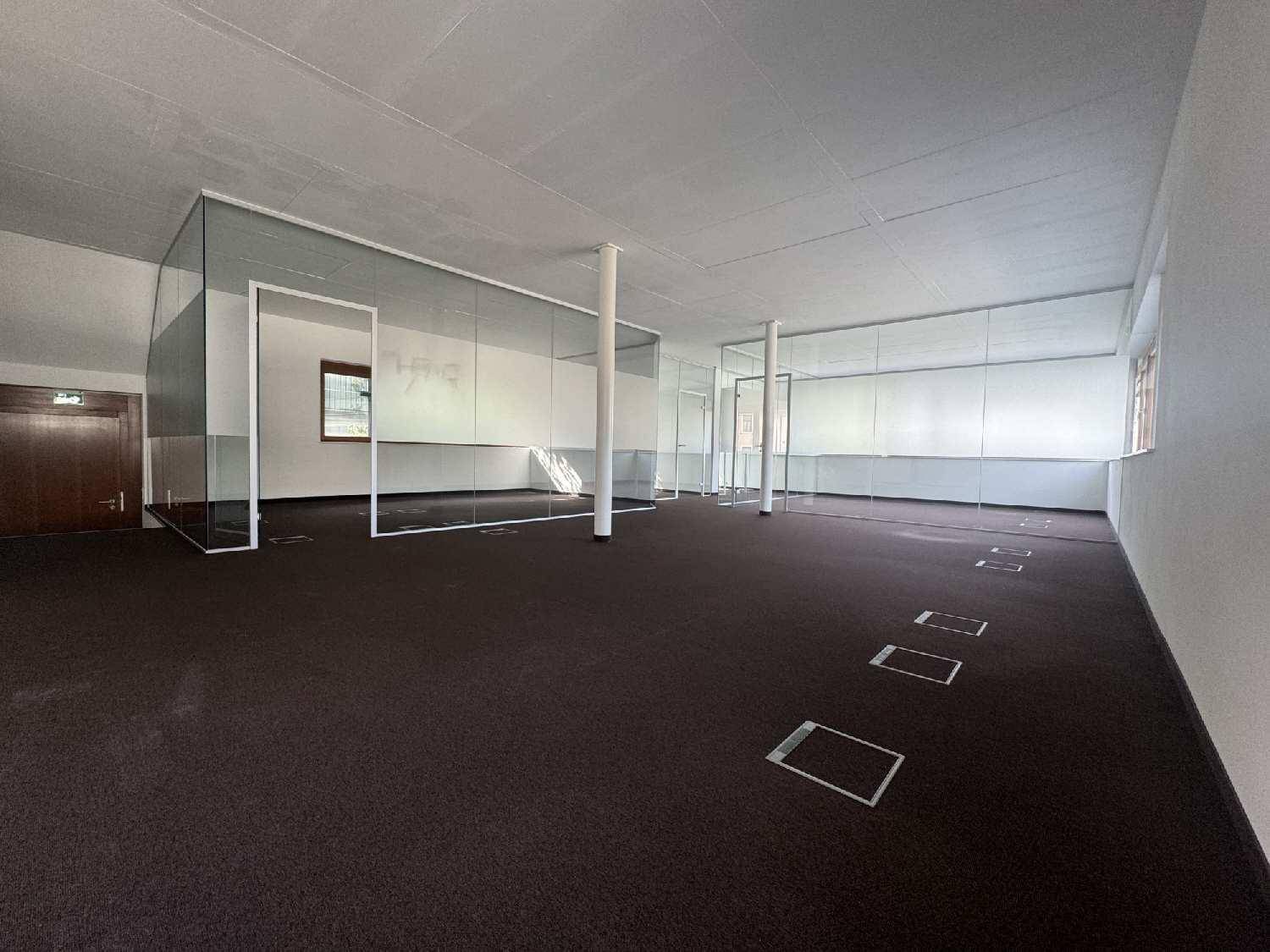 Weitläufiger Bürobereich mit dunklem Teppichboden, Glasabtrennungen und Bodentanks für Strom und Daten.