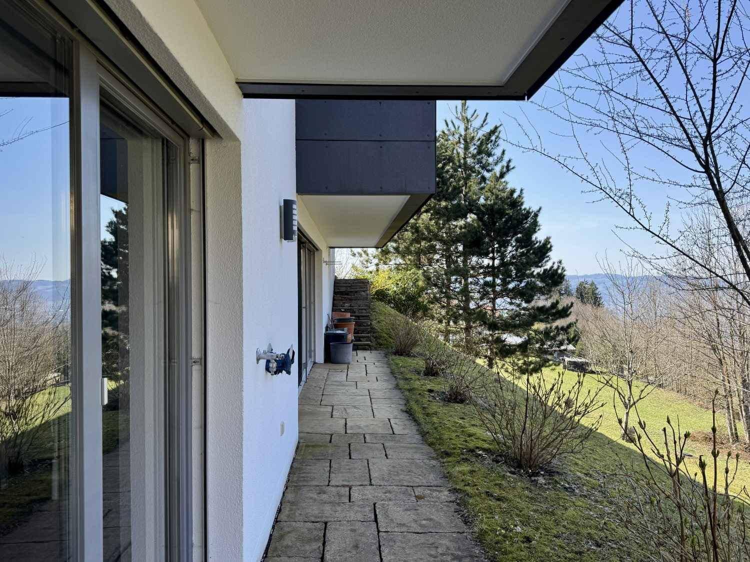 Seitlicher Zugang zum Haus mit gepflastertem Weg und Blick auf die umliegende Natur.