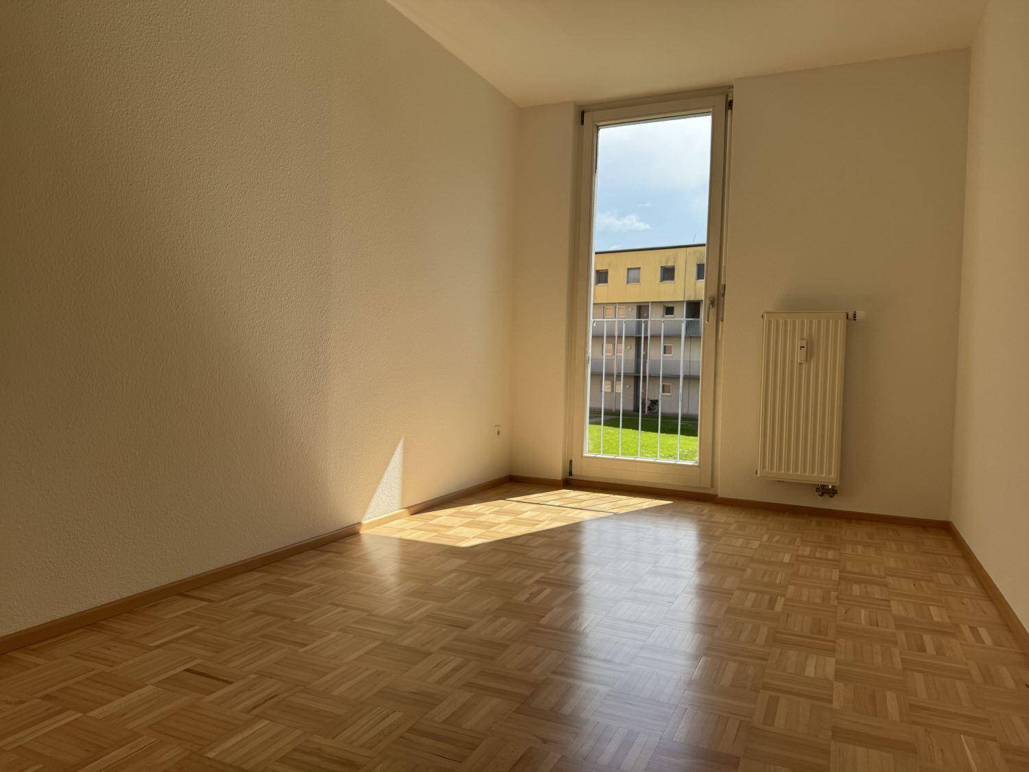 Helles Schlafzimmer mit Parkettboden und großem Fenster mit Blick ins Grüne.