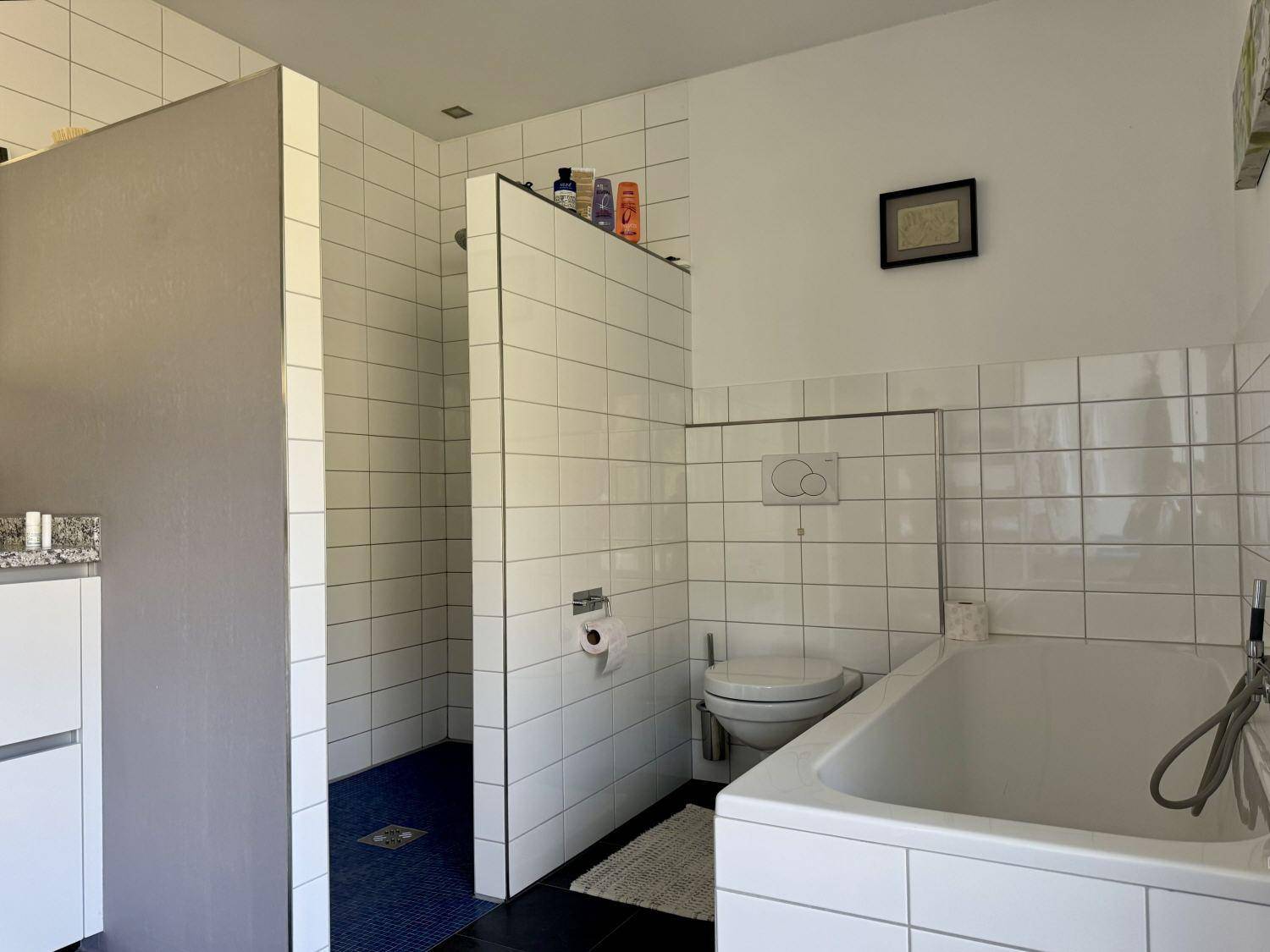 Modernes Badezimmer mit Badewanne, begehbarer Dusche und weißen Fliesen.