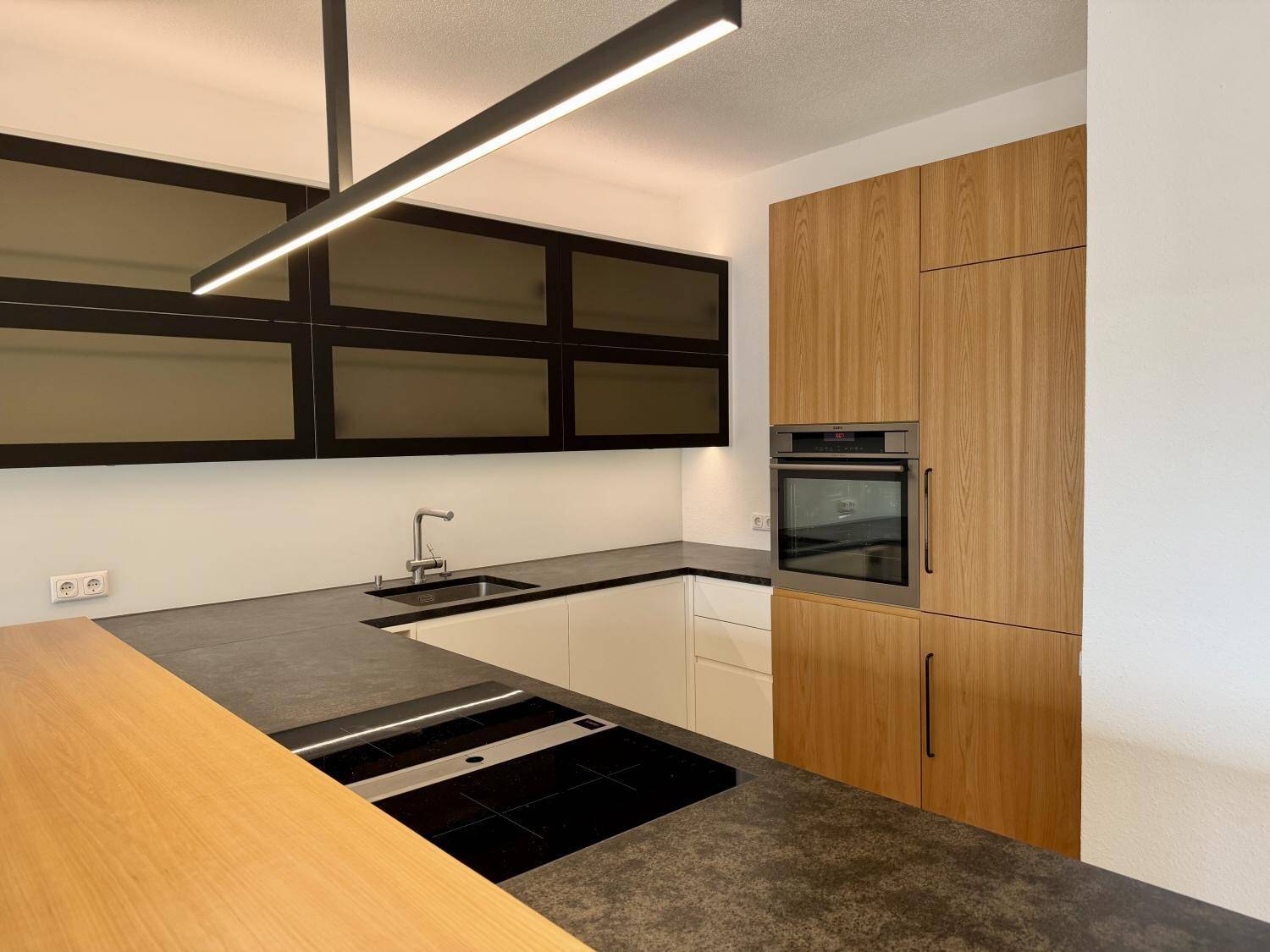 Gut ausgestattete Küche mit Induktionskochfeld, Backofen und eleganten Holzschränken.