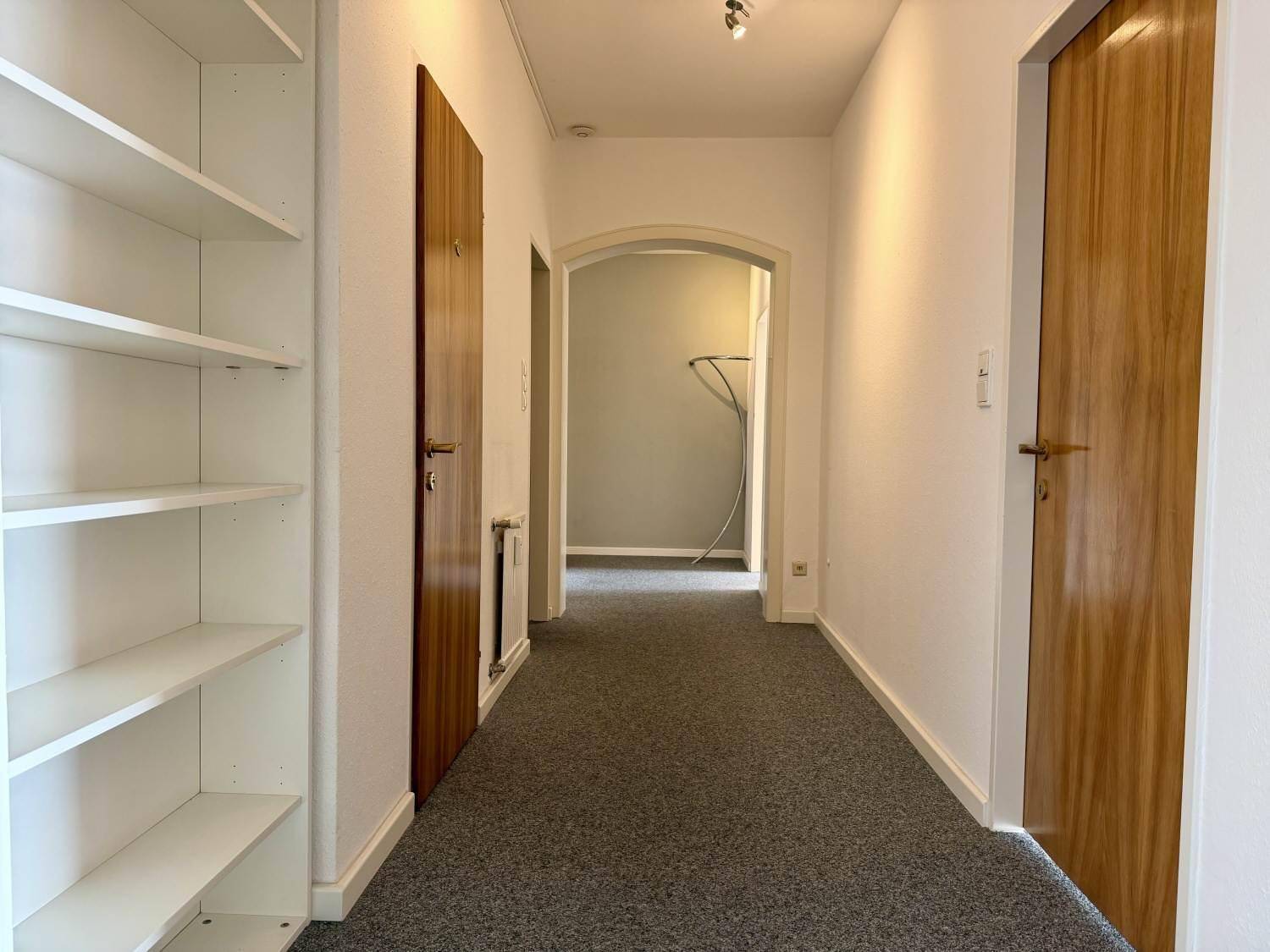 Heller Flur mit Teppichboden, Holztüren und einem praktischen Bücherregal.