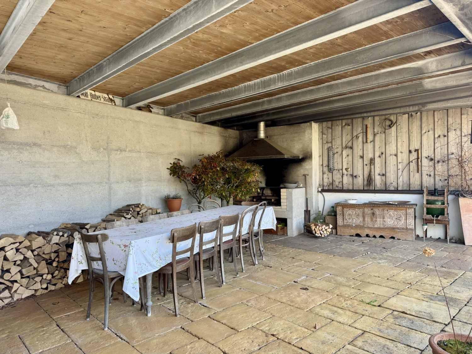 Überdachte Terrasse mit großem Esstisch, Außenkamin und Holzstapel.