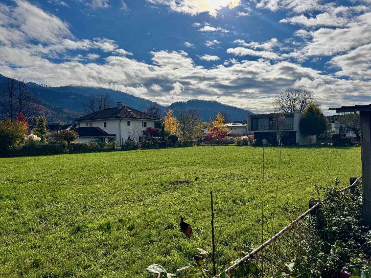 Sonnige Grünfläche mit Blick auf die Berge und umliegende Bebauung an einem klaren Herbsttag.