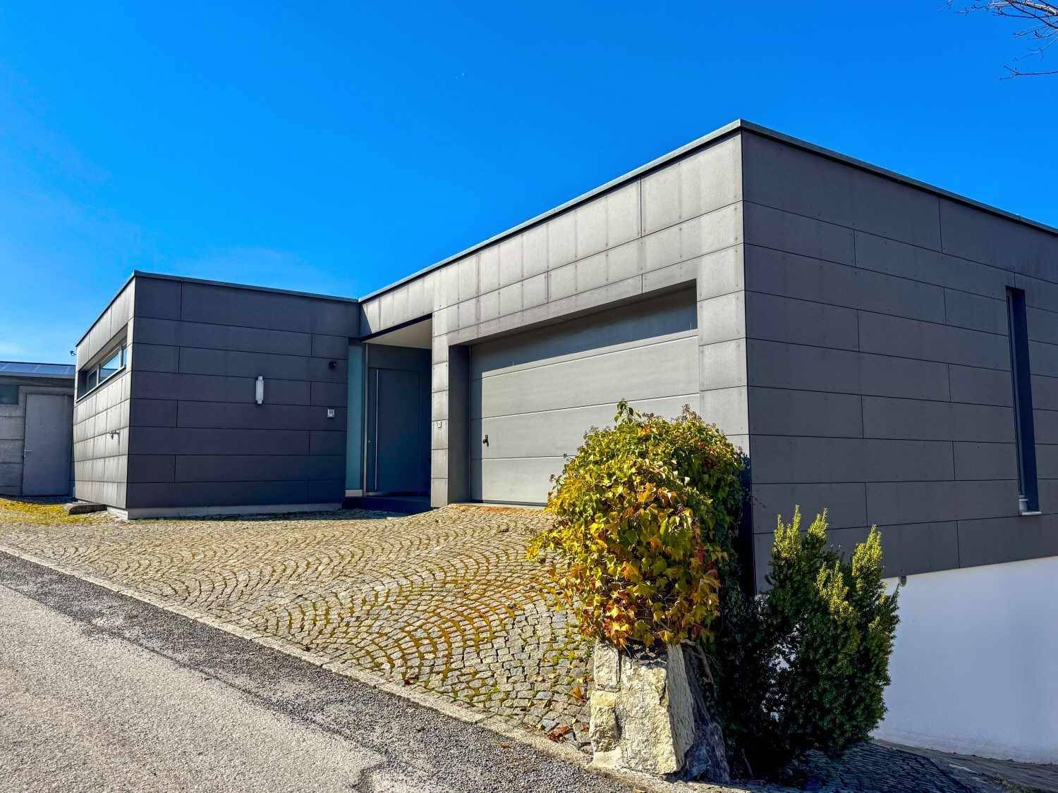 Modernes Haus mit integrierter Garage, grauer Fassade und gepflasterter Zufahrt.