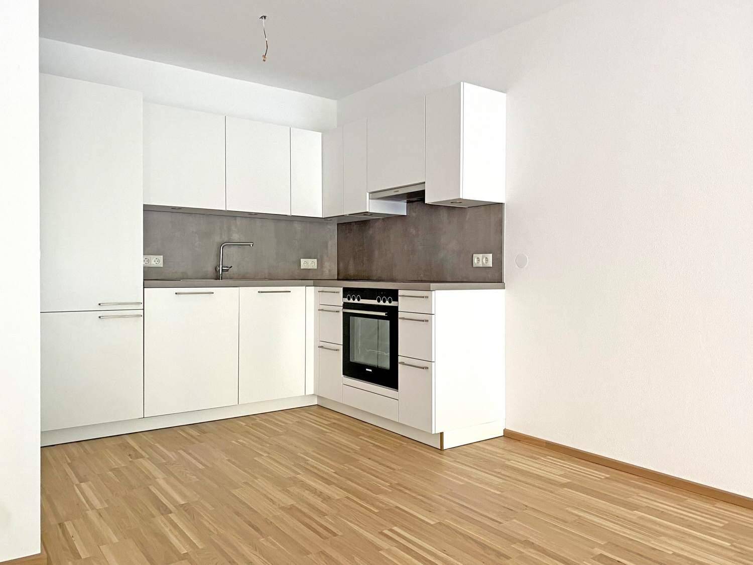 Moderne Einbauküche mit weißen Schränken, grauer Arbeitsplatte und integriertem Backofen.