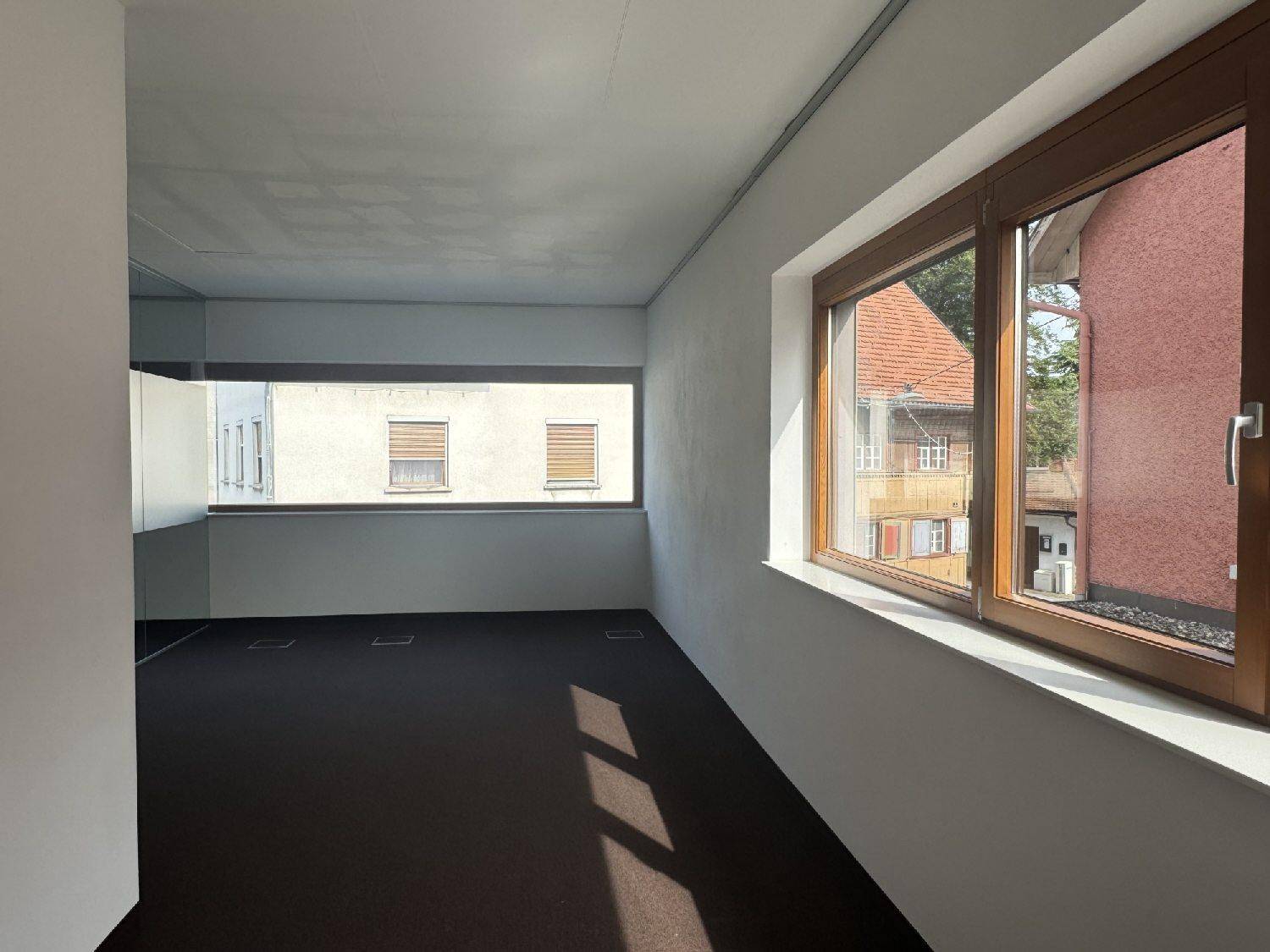 Geräumiges Büro mit Teppichboden, großen Holzfenstern und viel natürlichem Licht, das den Raum erhellt.