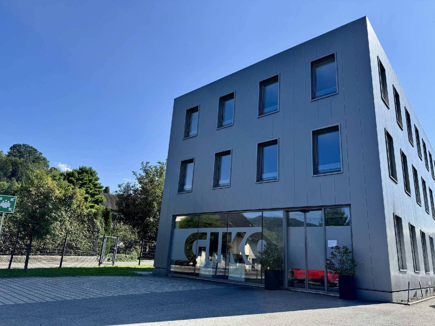 Modernes Bürogebäude mit grauer Fassade und großen Fenstern unter blauem Himmel.