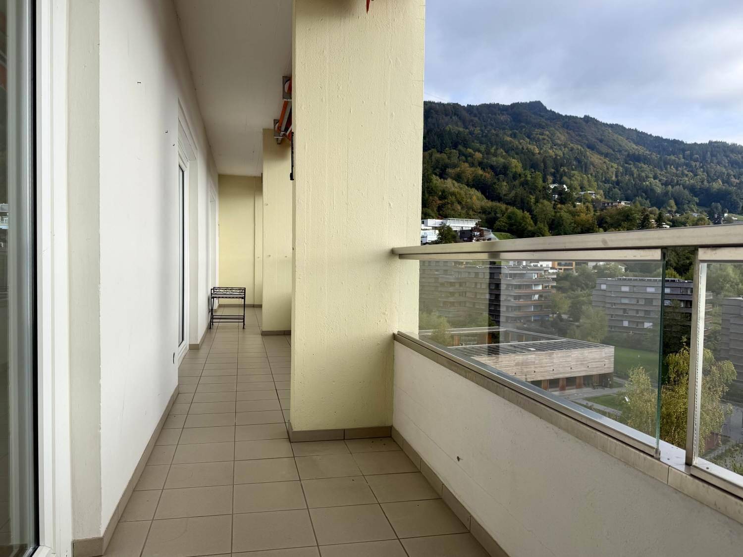 Geräumiger Balkon mit Fliesenboden und Blick auf grüne Hügel und umliegende Gebäude.