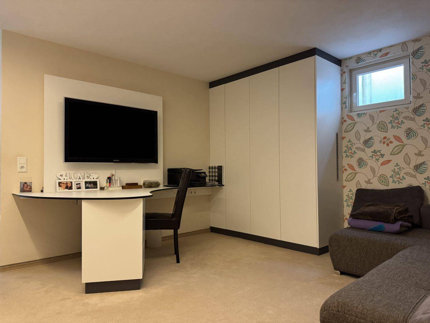 Geräumiges Zimmer mit Einbauschränken, Schreibtisch und floraler Tapete.
