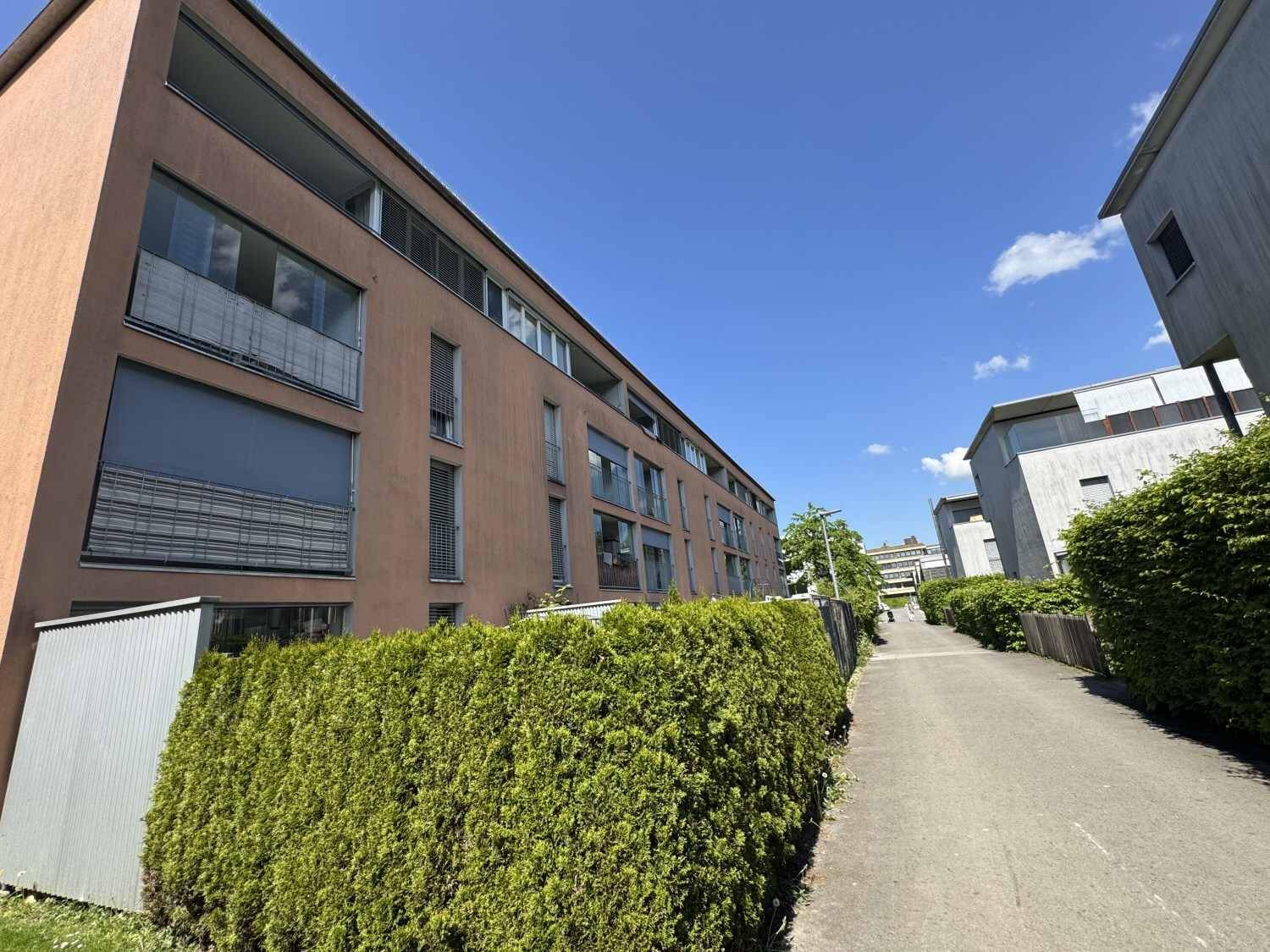 Moderne Wohngebäude mit gepflegten Hecken und einem Gehweg unter blauem Himmel.