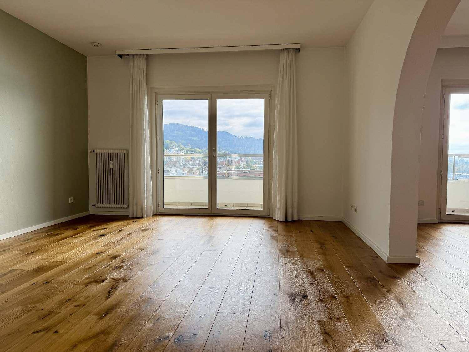 Helles Wohnzimmer mit Eichenparkett, einer Akzentwand und Zugang zu einem Balkon.