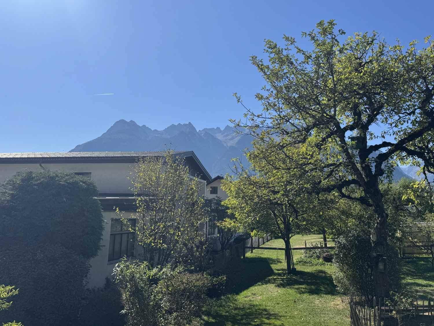 Malerischer Bergblick über grüne Bäume und Dächer an einem klaren, sonnigen Tag.