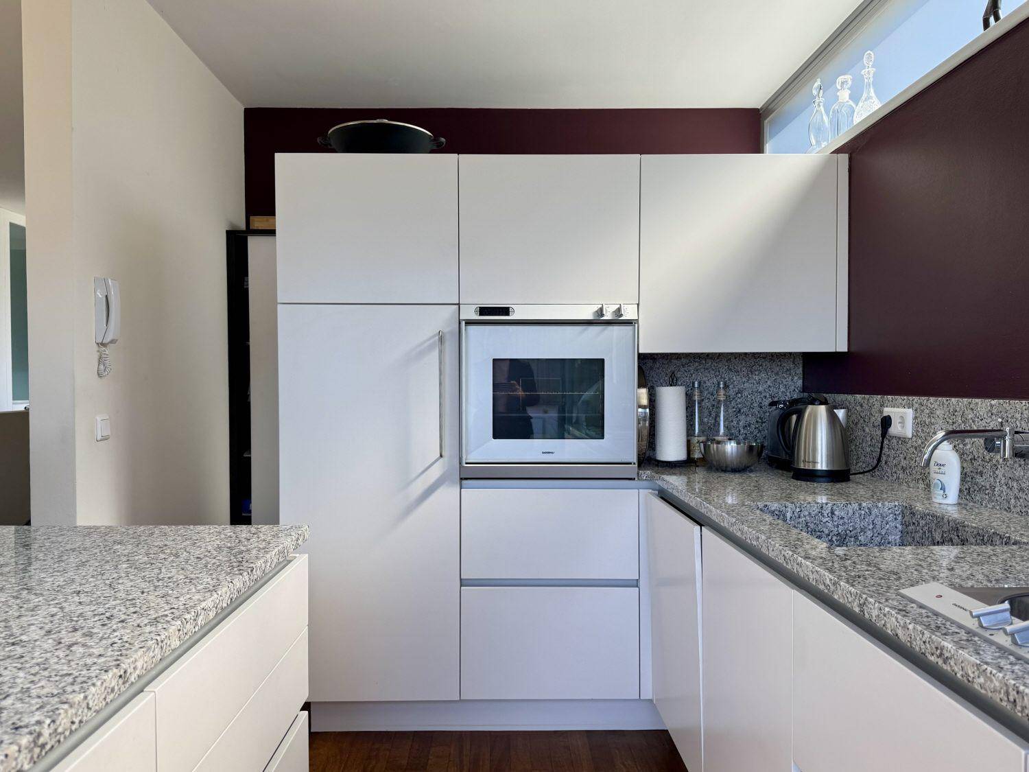Moderne Einbauküche mit weißen Schränken, Granitarbeitsplatten und integriertem Backofen.