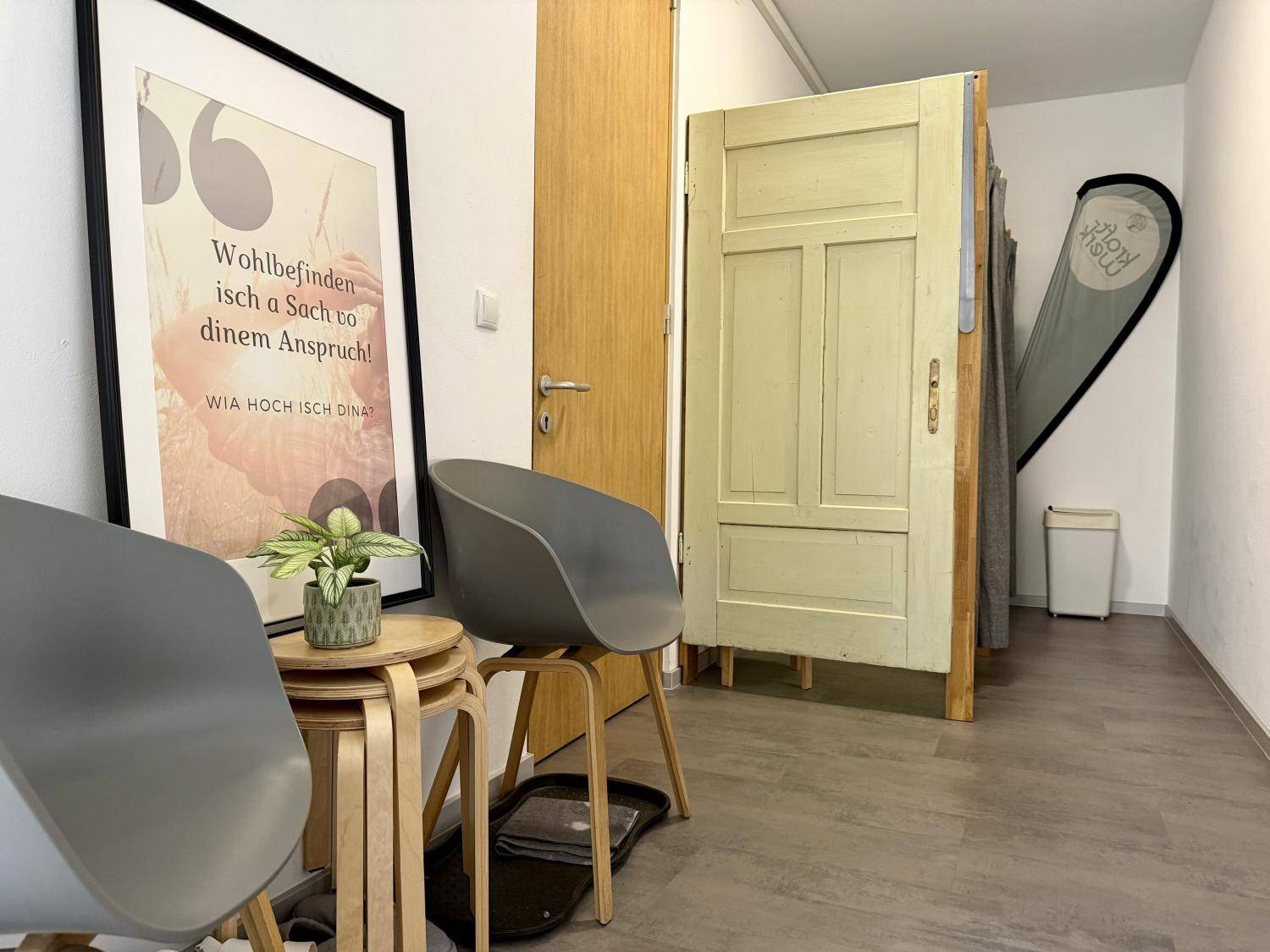 Empfangsbereich mit modernen Stühlen, einem kleinen Holztisch und einer praktischen Umkleidekabine für Besucher.