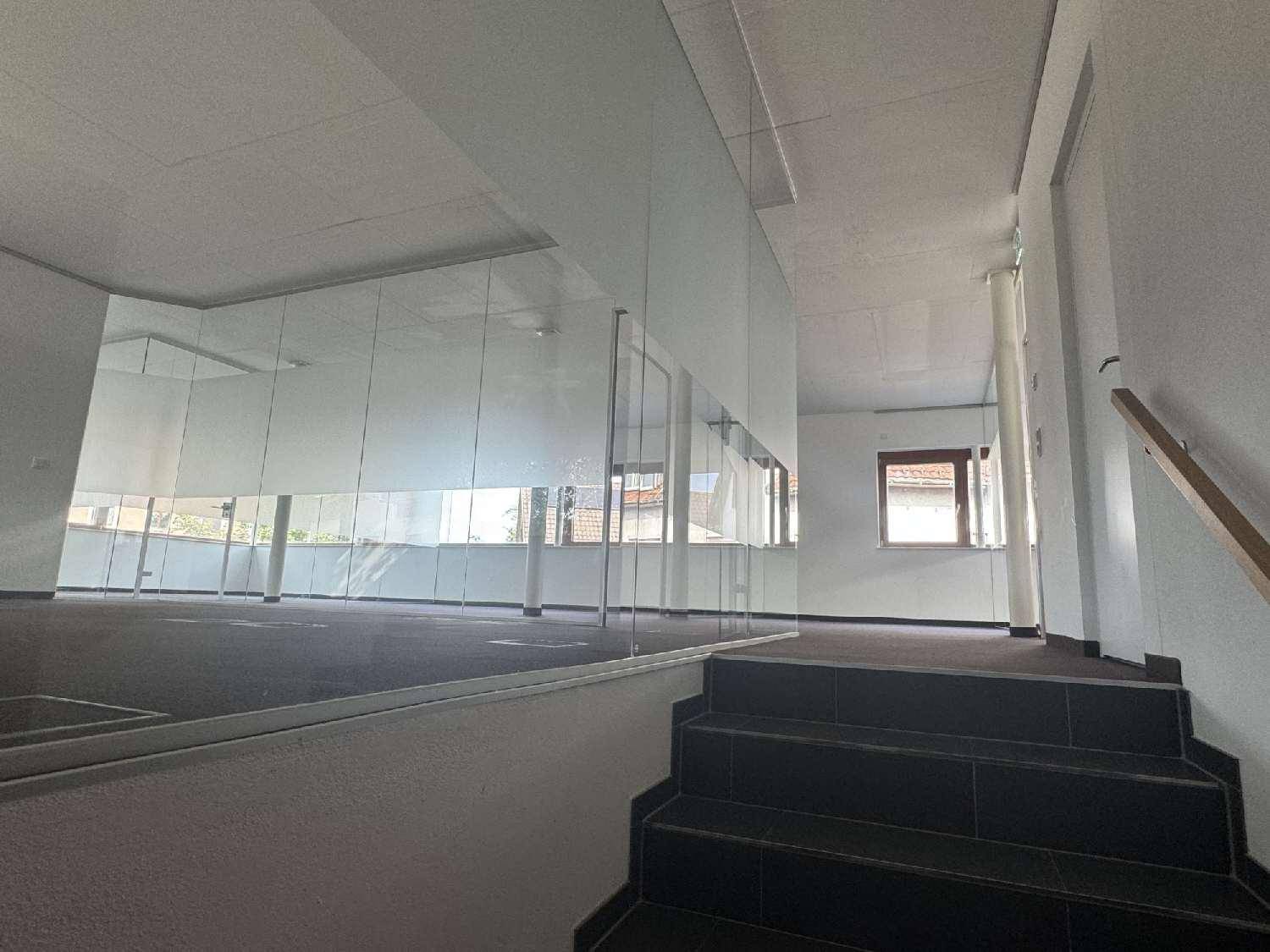 Innenansicht eines Bürobereichs mit dunkler Treppe, Glaswänden und Blick auf die Umgebung durch die Fenster.