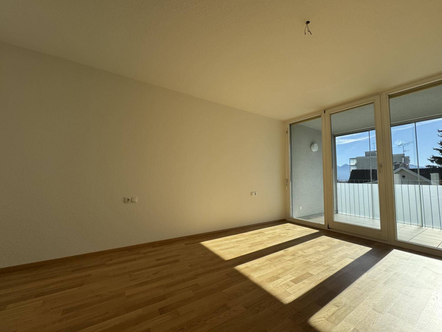 Heller Raum mit Parkettboden und großem Schiebefenster zum Balkon, bietet viel Sonnenlicht.