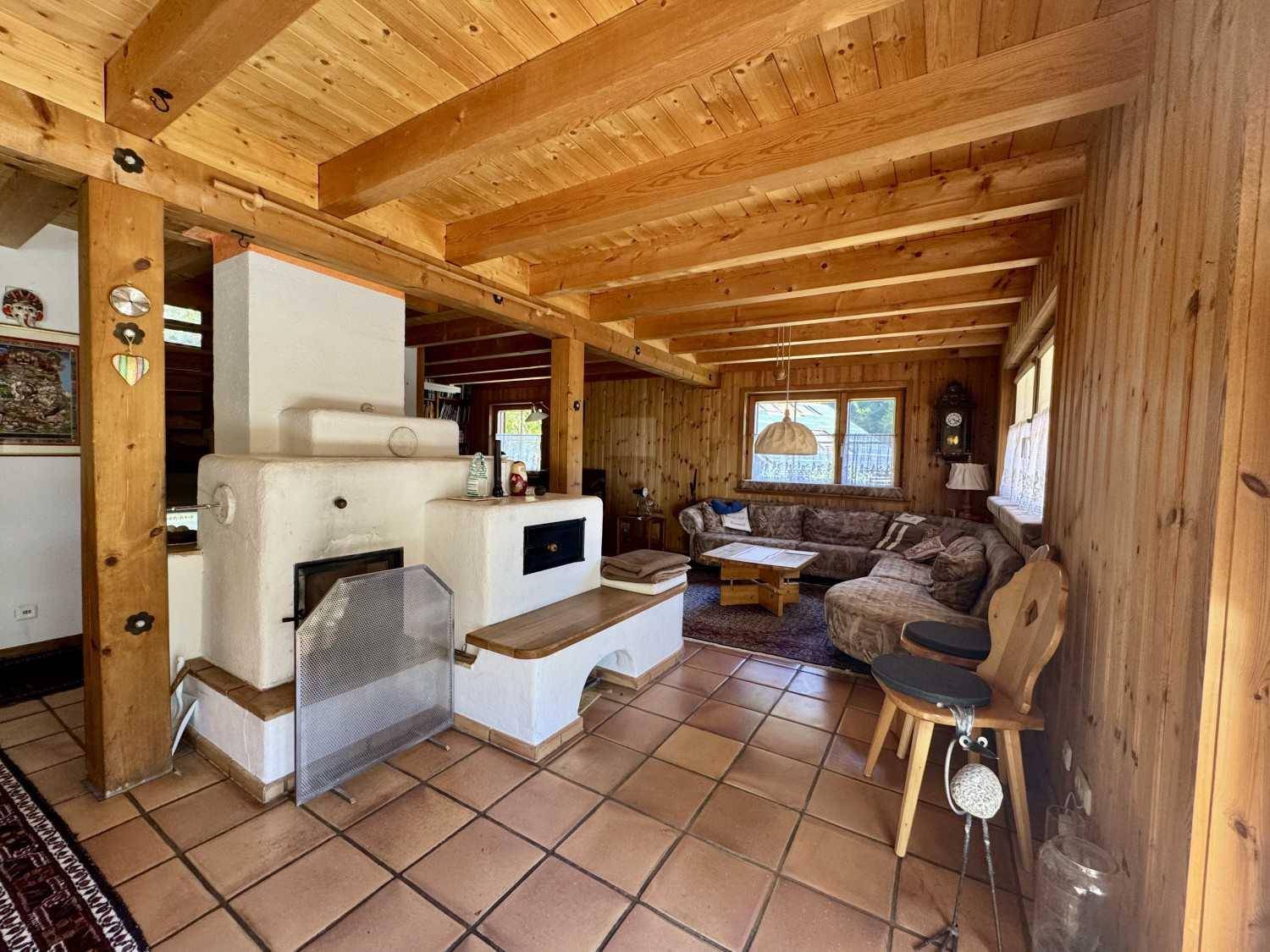 Rustikales Wohnzimmer mit Kachelofen, Holzbalkendecke und Terrakottafliesen.