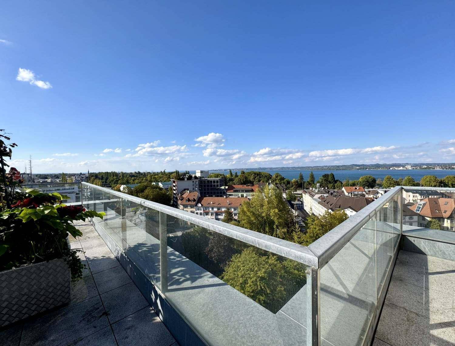 Weitläufiger Blick von der Dachterrasse über die Stadt und den See mit moderner Glasbrüstung.